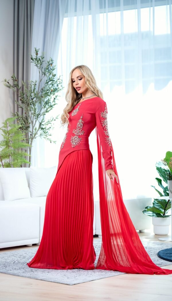 Model wearing a red couture gown with crystal-embellished bodice, pleated skirt, and sheer sleeve panels – Casa Reina Couture