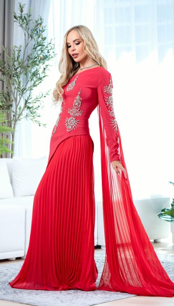 Model wearing a red couture gown with crystal-embellished bodice, pleated skirt, and sheer sleeve panels – Casa Reina Couture