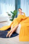Model wearing a golden yellow couture off-shoulder gown with hand-embroidered embellishments and dramatic cape panels – Casa Reina Couture