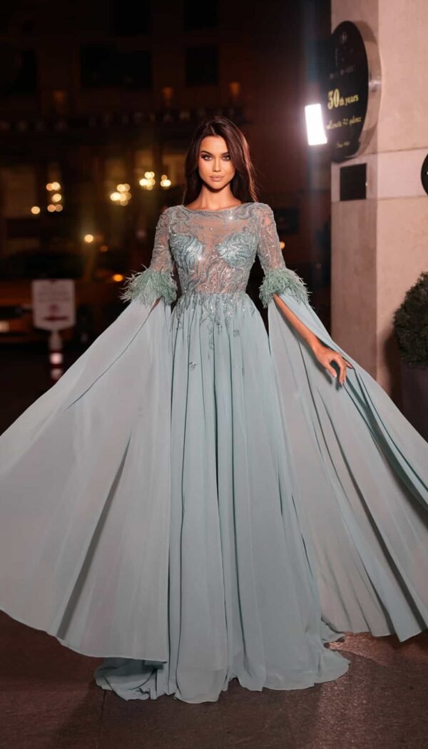 Model wearing a light blue evening gown with a sheer embellished bodice, long sleeves with flowing cape panels, and white feather accents at the cuffs – Casa Reina couture.