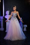 Model wearing a pastel pink evening gown with multicolored floral embellishments and layered tulle skirt – Casa Reina couture fashion.