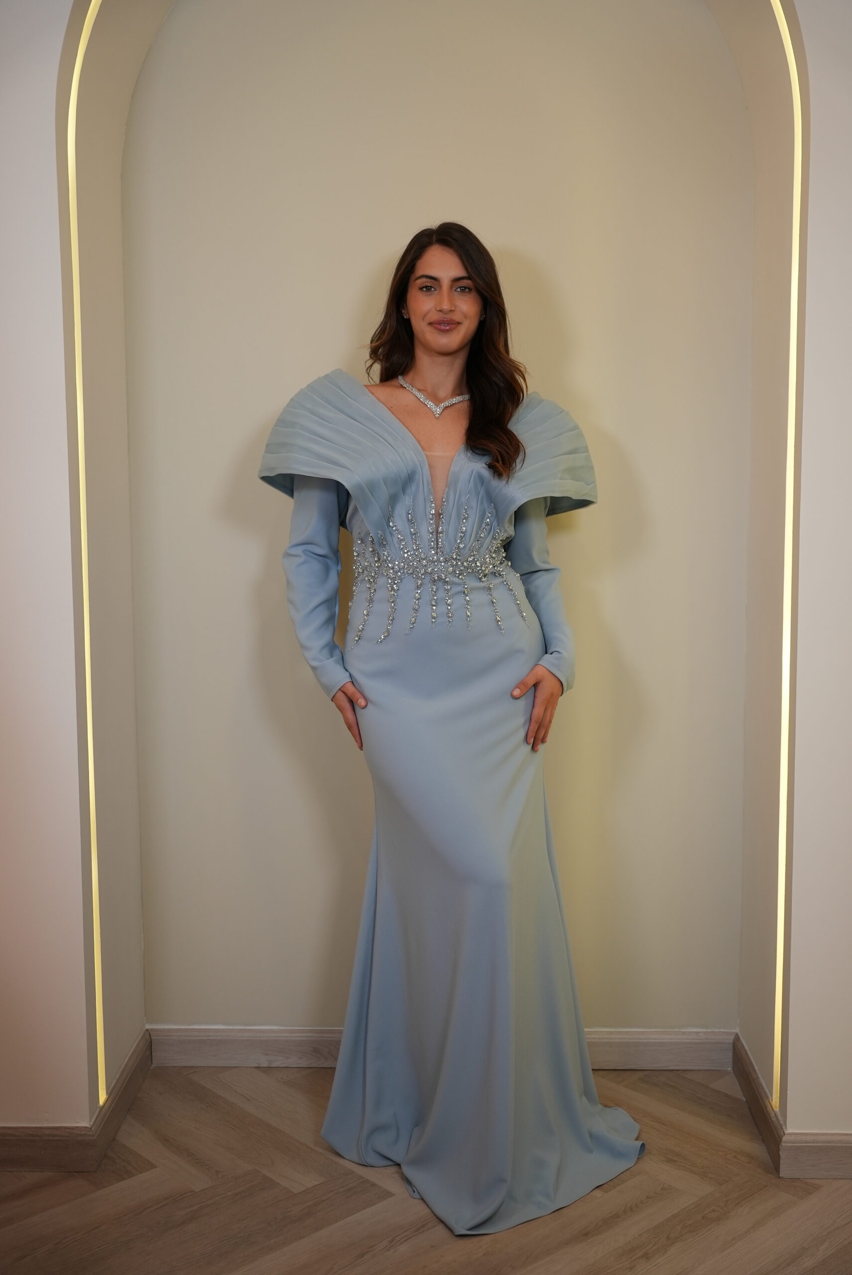 Model wearing a powder blue ready-to-wear evening gown with structured pleated shoulders and crystal embellishments – Casa Reina Boutique