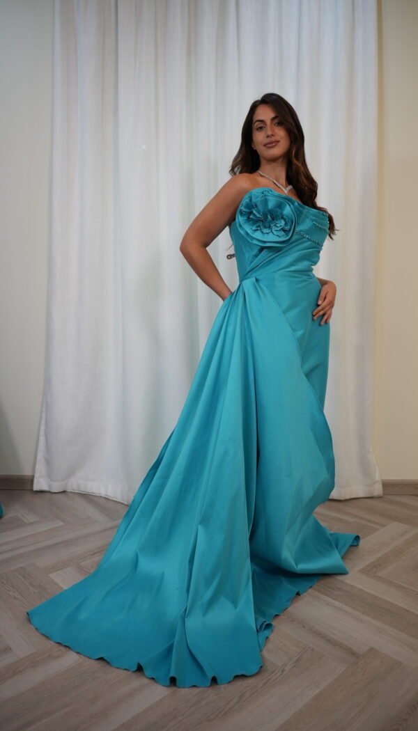Model wearing a turquoise one-shoulder evening gown with floral appliqué, bead detailing, and dramatic side drape with train – Casa Reina Boutique