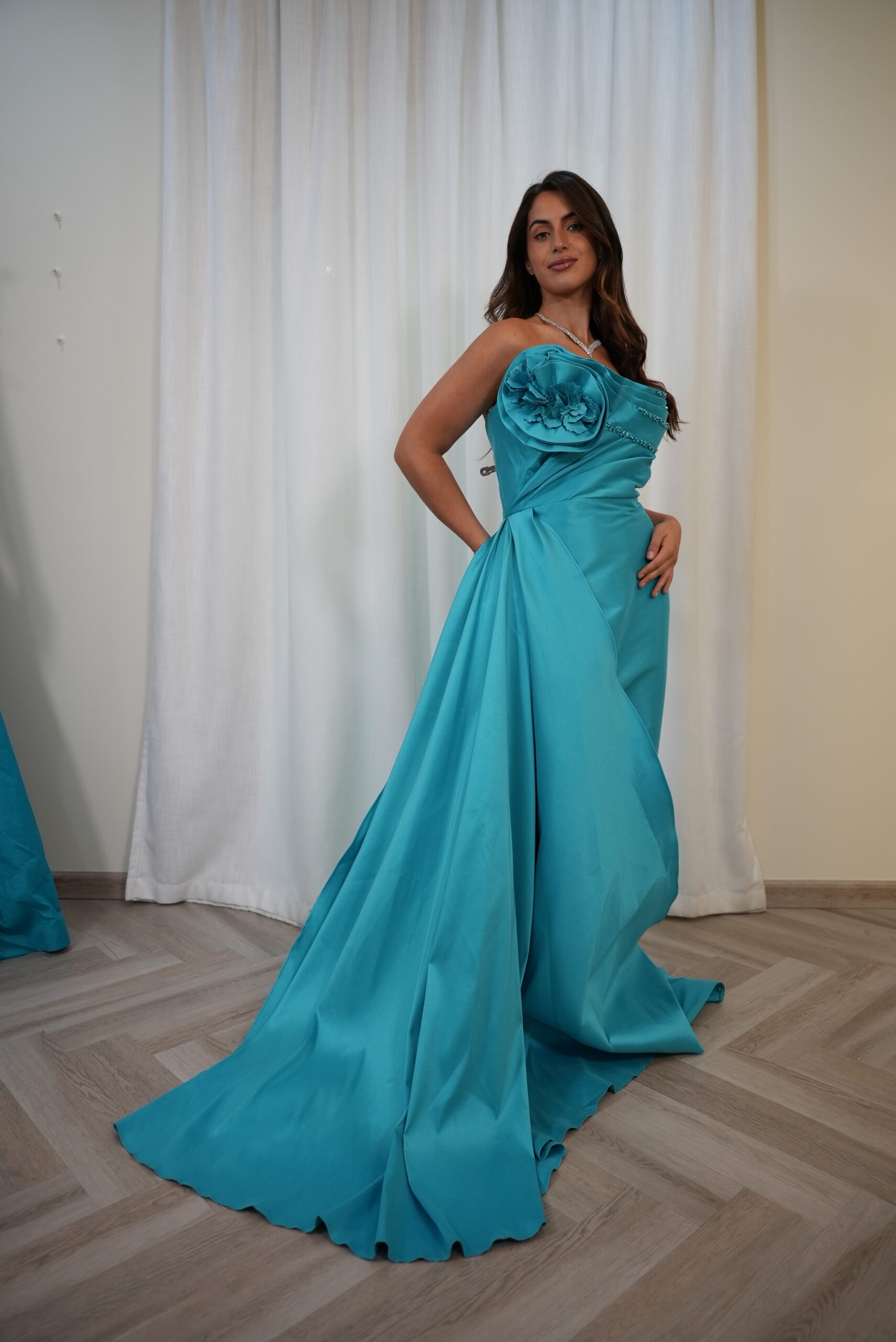 Model wearing a turquoise one-shoulder evening gown with floral appliqué, bead detailing, and dramatic side drape with train – Casa Reina Boutique