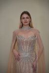 Model wearing a crystal-embellished illusion corset gown with vertical beadwork and flowing chiffon cape in Nude Beige – Casa Reina Boutique