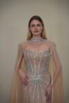 Model wearing a crystal-embellished illusion corset gown with vertical beadwork and flowing chiffon cape in Nude Beige – Casa Reina Boutique
