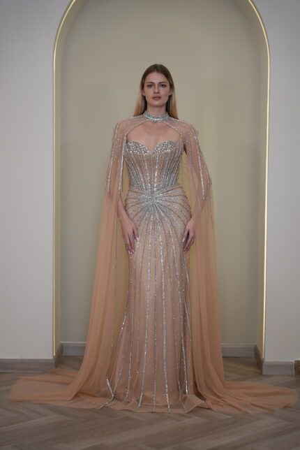 Model wearing a crystal-embellished illusion corset gown with vertical beadwork and flowing chiffon cape in Nude Beige – Casa Reina Boutique