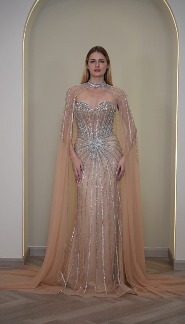 Model wearing a crystal-embellished illusion corset gown with vertical beadwork and flowing chiffon cape in Nude Beige – Casa Reina Boutique