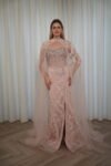 Model wearing a blush evening gown with crystal embellishments, strapless bodice, and sheer embroidered cape – Casa Reina Boutique