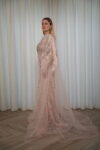 Model wearing a blush evening gown with crystal embellishments, strapless bodice, and sheer embroidered cape – Casa Reina Boutique