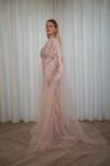 Model wearing a blush evening gown with crystal embellishments, strapless bodice, and sheer embroidered cape – Casa Reina Boutique
