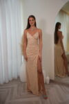 Model wearing a sequin spaghetti strap evening gown with V-neckline, ruched waist, and thigh-high slit, available in champagne – Casa Reina couture collection.