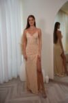 Model wearing a sequin spaghetti strap evening gown with V-neckline, ruched waist, and thigh-high slit, available in champagne – Casa Reina couture collection.