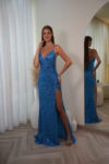 Model wearing a sequin spaghetti strap evening gown with V-neckline, ruched waist, and thigh-high slit, available in blue – Casa Reina couture collection.