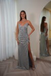 Model wearing a sequin spaghetti strap evening gown with V-neckline, ruched waist, and thigh-high slit, available in silver – Casa Reina couture collection.