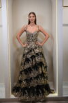 Model wearing a black and gold tiered floral embroidered evening gown with sweetheart neckline and layered skirt – Casa Reina couture fashion.