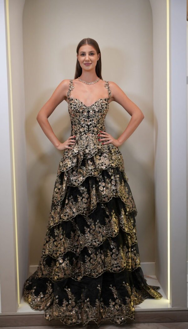 Model wearing a black and gold tiered floral embroidered evening gown with sweetheart neckline and layered skirt – Casa Reina couture fashion.