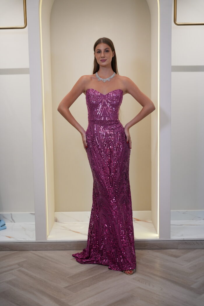 Model wearing a magenta strapless sequin evening gown with sweetheart neckline, detachable puff sleeves, and flowing cape – Casa Reina couture collection.