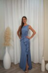 Model wearing a sleeveless evening gown with bateau neckline, draped waist, side ruffle, and thigh-high slit, available in slate blue – Casa Reina couture collection.