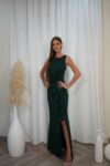 Model wearing a sleeveless evening gown with bateau neckline, draped waist, side ruffle, and thigh-high slit, available in emerald green – Casa Reina couture collection.