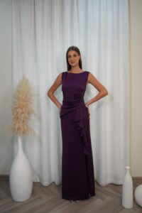Model wearing a sleeveless evening gown with bateau neckline, draped waist, side ruffle, and thigh-high slit, available in plum – Casa Reina couture collection.