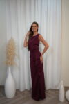 Model wearing a sleeveless evening gown with bateau neckline, draped waist, side ruffle, and thigh-high slit, available in burgundy – Casa Reina couture collection.