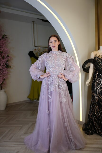 Model wearing a lavender embroidered tulle evening gown with high neckline, sheer puff sleeves, and floral appliqué – Casa Reina couture collection.
