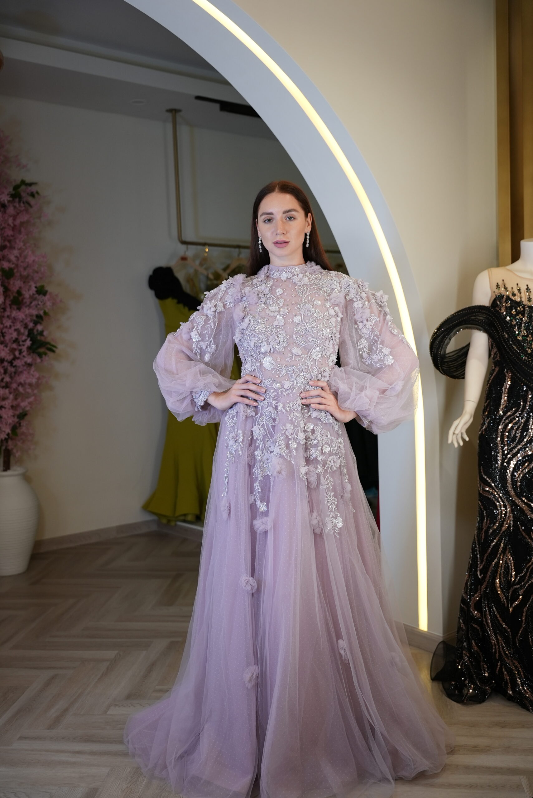 Model wearing a lavender embroidered tulle evening gown with high neckline, sheer puff sleeves, and floral appliqué – Casa Reina couture collection.