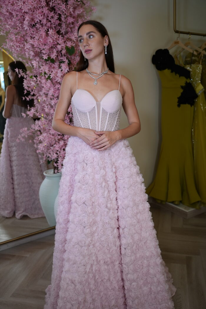 Model wearing a pink corset evening gown with embellished bodice and 3D rosette skirt featuring a thigh-high slit – Casa Reina couture collection.