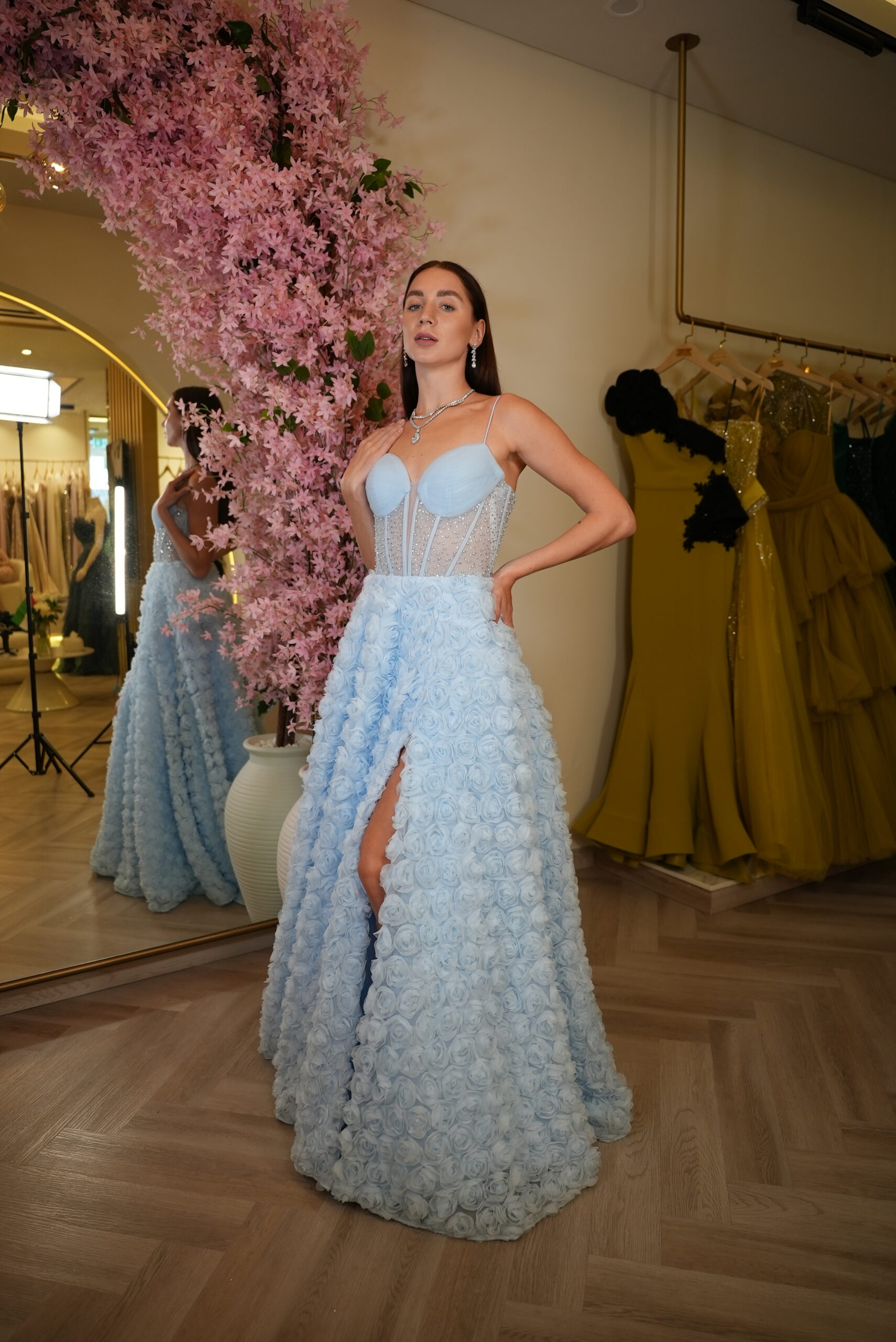 Model wearing a powder blue corset evening gown with embellished bodice and 3D rosette skirt featuring a thigh-high slit – Casa Reina couture collection.