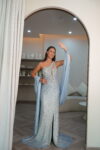 Model wearing a one-shoulder evening gown with a high thigh slit, all-over sequin embellishments, and a long draped shawl from the arm, available in powder blue color – Casa Reina couture.