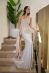 Model wearing a champagne one-shoulder evening gown with crystal embellishments, thigh-high slit, and draped shawl – Casa Reina Boutique