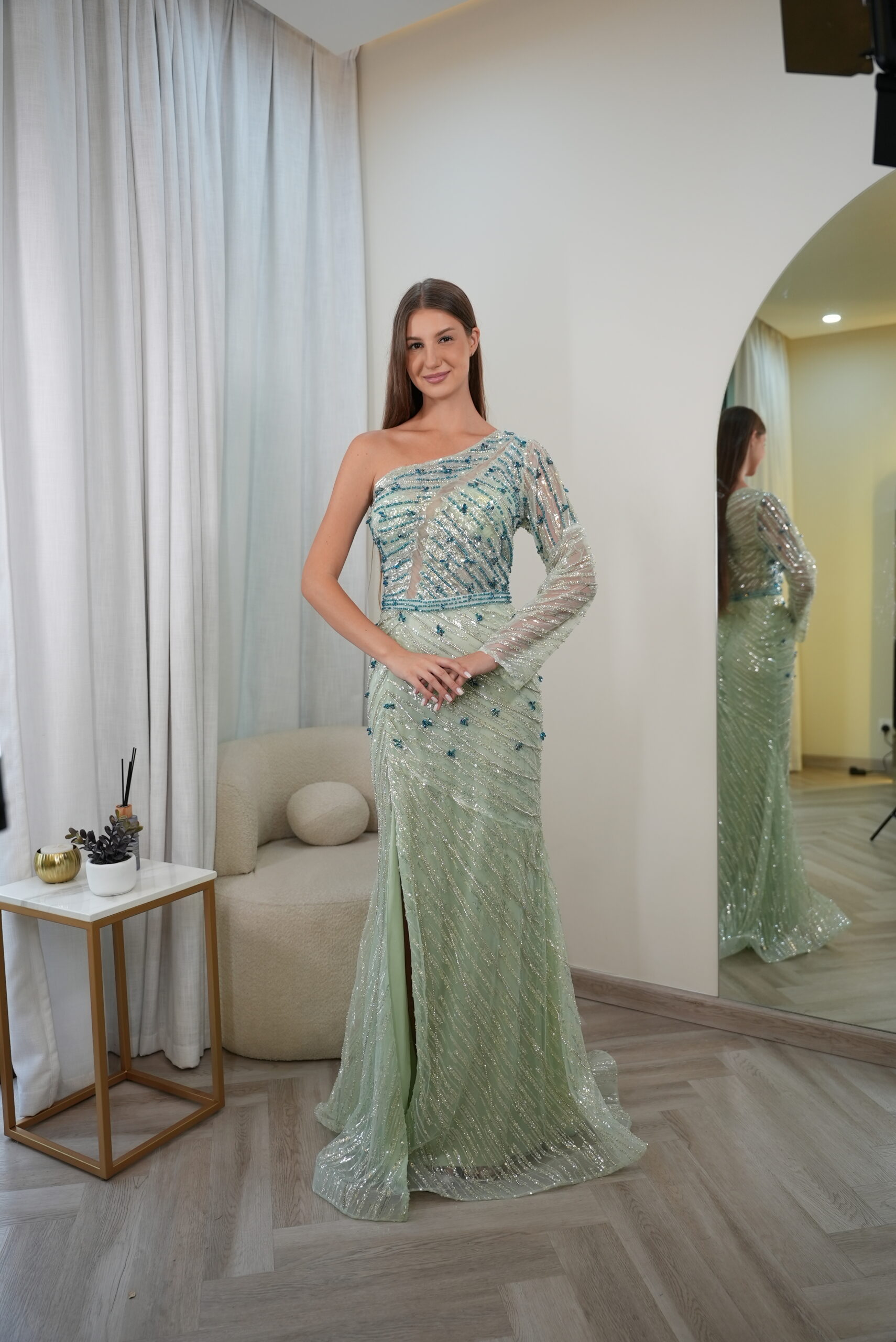 Model wearing a mint green one-shoulder gown with silver and aqua sequins, sheer embellished sleeve, and slit skirt – Casa Reina Boutique