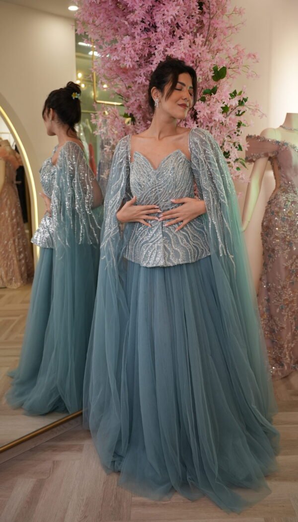 Model wearing a dusty blue evening gown with beaded sweetheart bodice, shimmering cape sleeves, and voluminous layered tulle skirt – Casa Reina Boutique