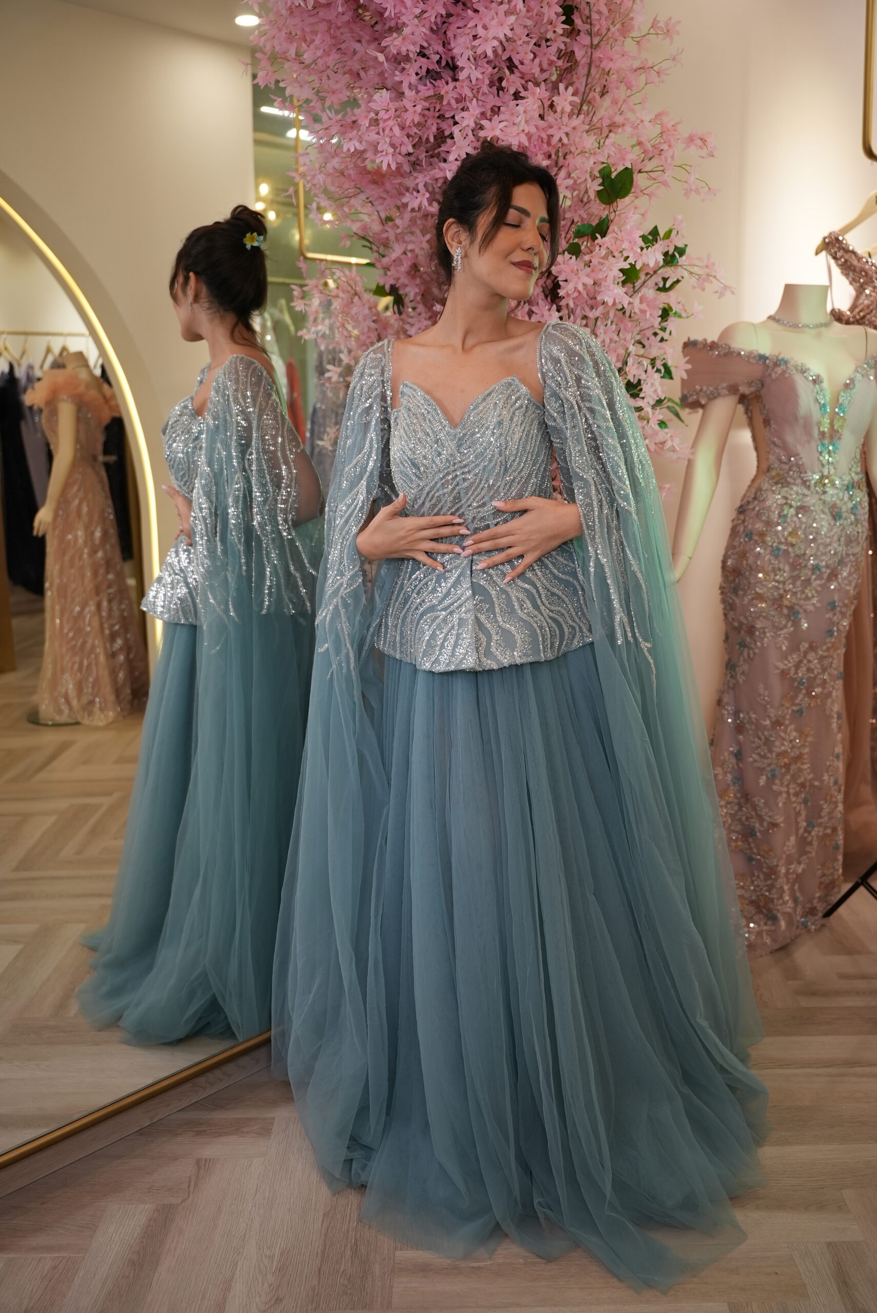 Model wearing a dusty blue evening gown with beaded sweetheart bodice, shimmering cape sleeves, and voluminous layered tulle skirt – Casa Reina Boutique
