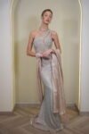 Model wearing a one-shoulder evening gown with a high thigh slit, all-over sequin embellishments, and a long draped shawl from the arm, available in golden champagne color – Casa Reina couture.
