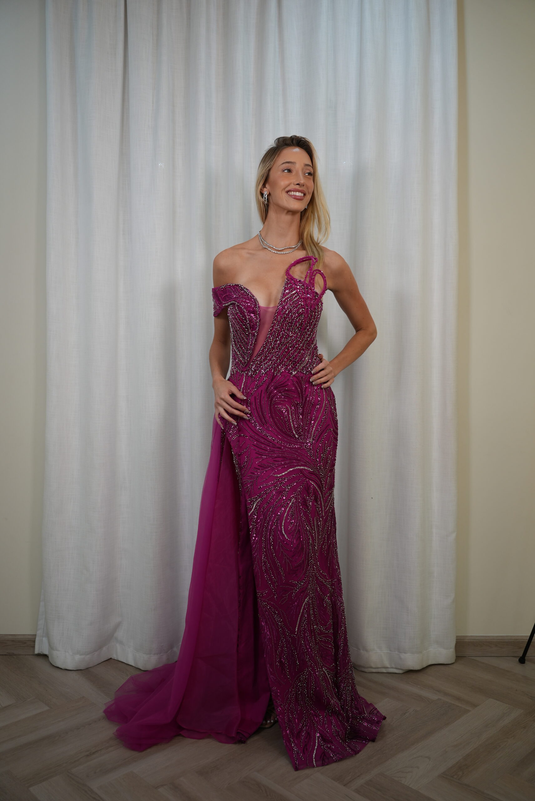 Model wearing a fuchsia evening gown with beaded illusion bodice, asymmetrical off-shoulder strap, and floor-length skirt with soft train – Casa Reina Boutique