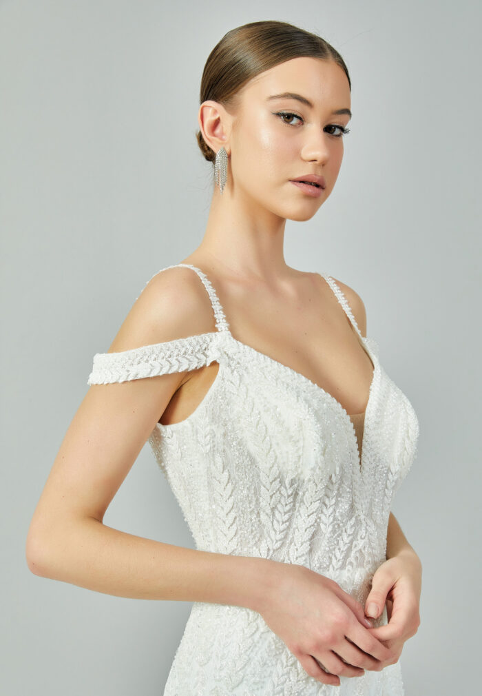 Bride wearing a beaded mermaid gown with illusion V-neckline and off-shoulder straps from Casa Reina Bridal Collection