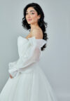 Bride wearing an off-shoulder sculpted organza ball gown with voluminous sleeves and pleated bodice from Casa Reina Bridal Collection