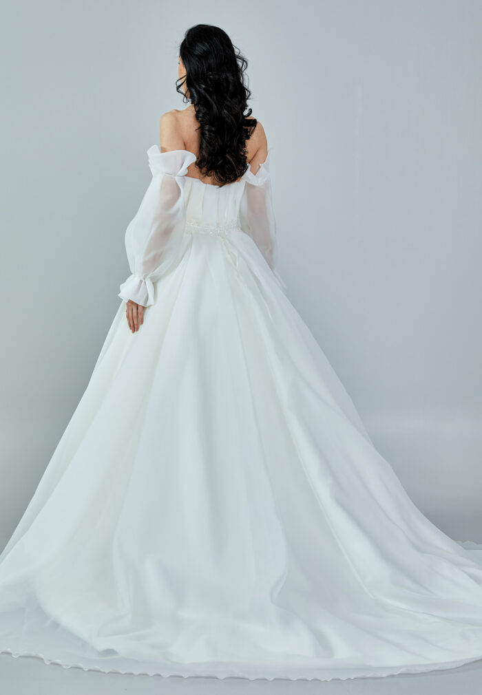 Bride wearing an off-shoulder sculpted organza ball gown with voluminous sleeves and pleated bodice from Casa Reina Bridal Collection