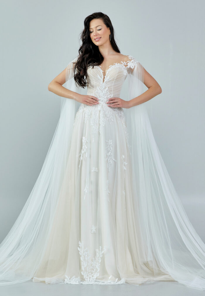 Bride wearing an ethereal tulle gown with illusion bodice, lace embroidery, and flowing cape sleeves from Casa Reina Bridal Collection
