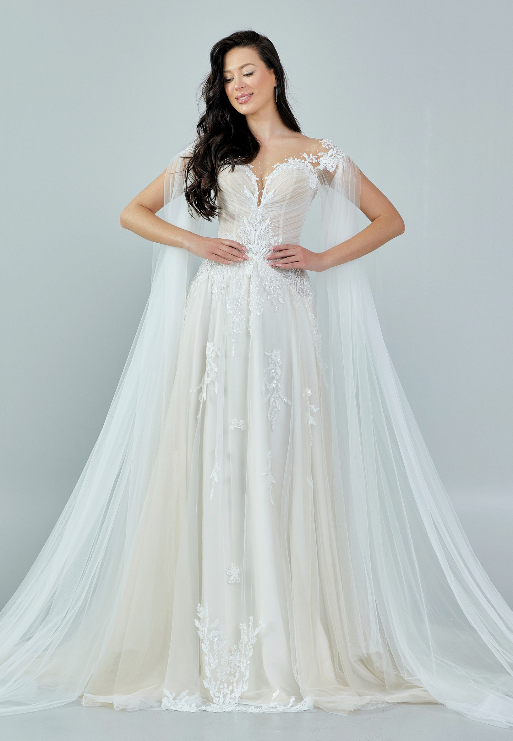 Bride wearing an ethereal tulle gown with illusion bodice, lace embroidery, and flowing cape sleeves from Casa Reina Bridal Collection