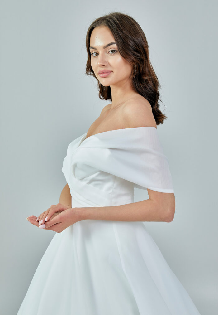 Bride wearing an off-shoulder organza ball gown with draped bodice and full skirt from Casa Reina Bridal Collection